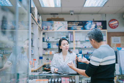 asian chinese senior man seeking advise from female pharmacist on medical supplies at drugstore pharmacy