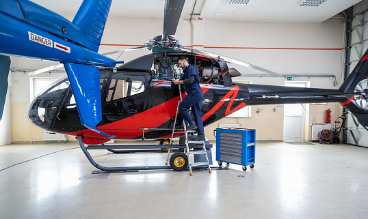 Aero mechanic fixing and checking a helicopter in hangar. Aviation and safety concept.