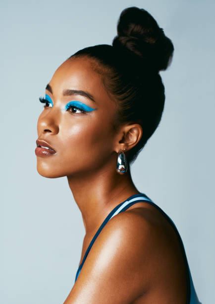 Beautiful african woman wearing fashion makeup in a studio against a grey background. Side profile of a woman looking away wearing sportswear and bright blue eyeshadow. Beauty and glamour Beautiful african woman wearing fashion makeup in a studio against a grey background. Side profile of a woman looking away wearing sportswear and bright blue eyeshadow. Beauty and glamour black woman hair bun stock pictures, royalty-free photos & images