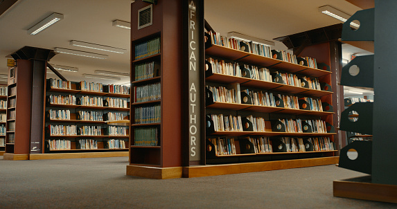 Happy tenage girl or student taking book from shelf in library - People, knowledge, education and school concept