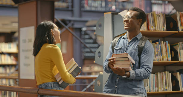 istock Interracial couple talking inside a library. Young man and woman doing research. Happy study partners doing a project 1401178592