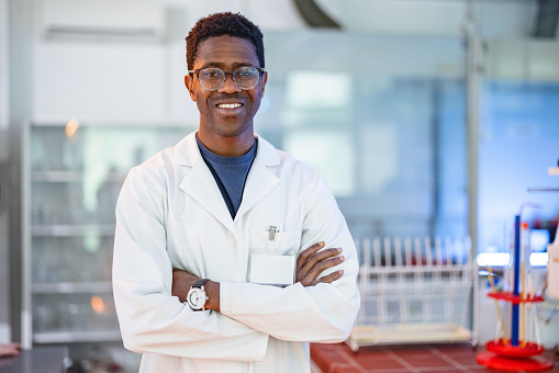 Smiling happy looking African-American male scientist standing in a laboratory and posing with arms crossed.