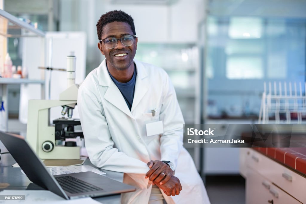 Young African-American Scientist Standing In Laboratory Happy looking African-American researcher wearing a lab coat, standing and posing in a laboratory. He is looking and smiling at the camera. Science Stock Photo