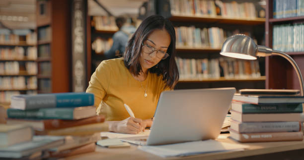 young lady using a laptop to do research on the internet. woman working on a project. mixed race woman sending emails. - library stockfoto's en -beelden