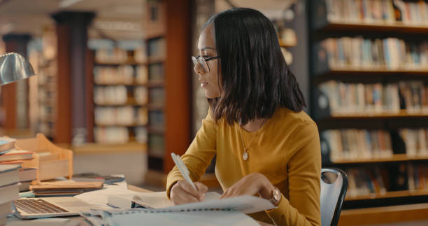 istock Mixed race woman doing research inside a library. Young lady working on a project alone. Woman sitting and writing in a book 1401178947