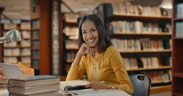 istock Happy woman sitting inside a library alone. Young lady working on a project looking at the camera. Mixed race woman smiling in a desk doing research 1401178949