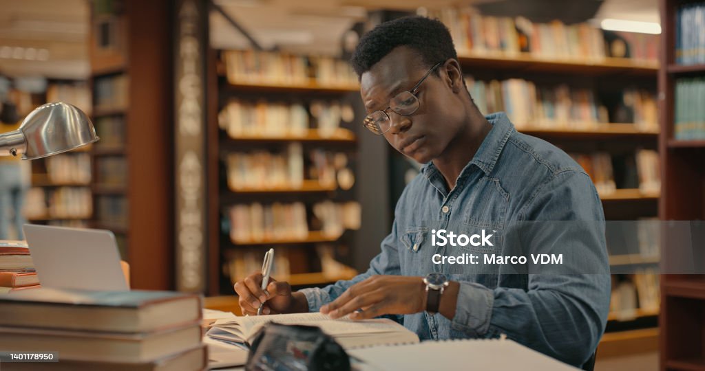 African man sitting inside a library alone doing research. Man working on a project. Young man doing research for a case. Lawyer working on a case Research Stock Photo