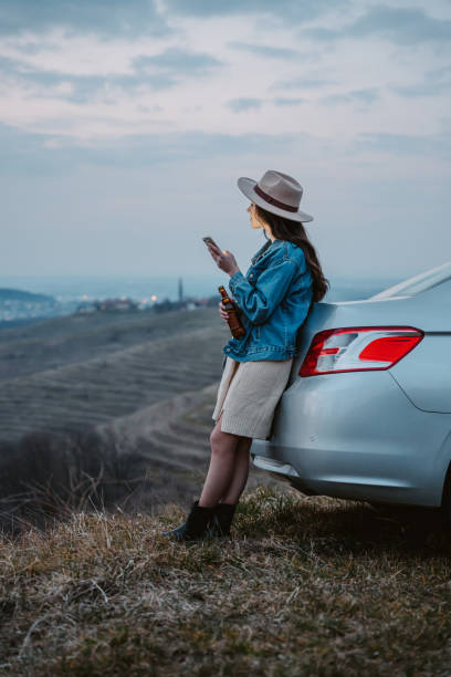 istock Young woman with beer bottle using cellphone while leaning on car trunk 1401179217