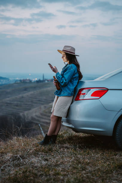 istock Young woman with beer bottle using cellphone while leaning on car trunk 1401179250