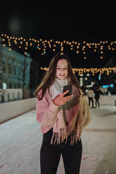 istock Young woman using mobile phone while standing on ice skate rink at night 1401179907
