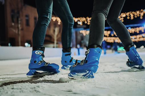 Young women legs in blue skates ice-skating together on outdoor rink at night