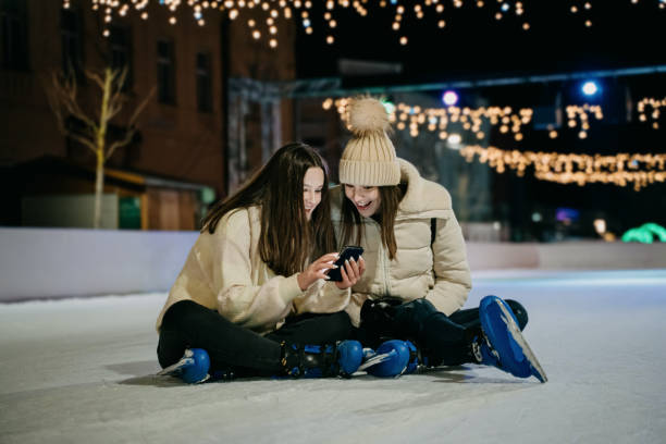 istock Happy young women seeing into mobile phone while sitting on skate rink at night 1401180076
