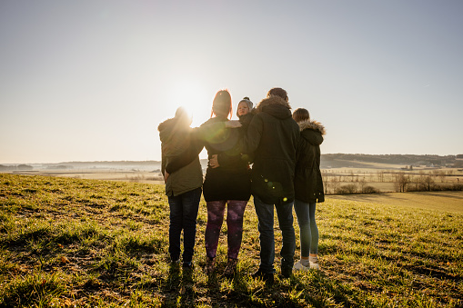 Parents with children embracing each other while standing in grassy field on sunny day