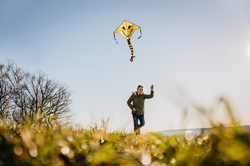 Smiling boy flying kite while running through green grassy field on sunny day