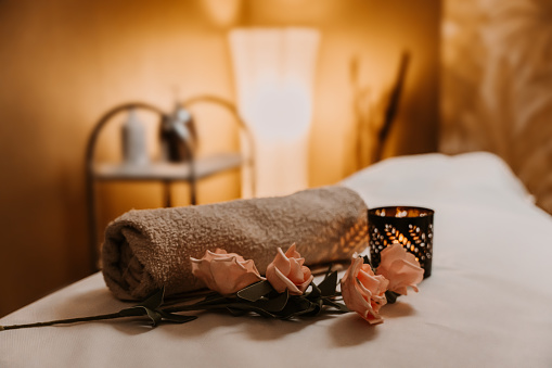 Close up of rolled towel, rose and burning candle decorated on bed at spa