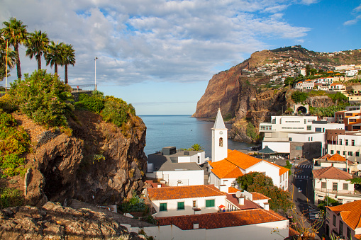 View of the town of Câmara de Lobos on Madeira Island, with cliffs, clouds and the sea in the background.