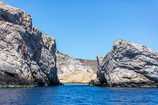 Cyclades Greece. Rock formation, cliff and cave, rippled Aegean Sea and blue sky, near Ios island