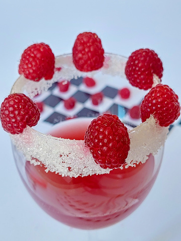 Glass cup decorated with raspberries and sugar in the background you can see table with figures like raspberries