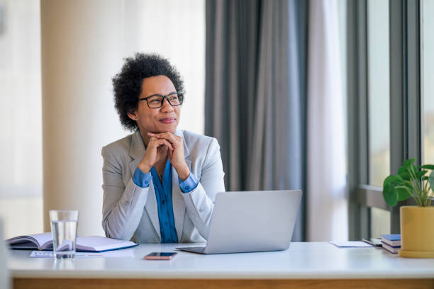 Thoughtful businesswoman wearing eyeglasses looking through window at desk Thoughtful mid adult businesswoman wearing eyeglasses looking through window at office desk one mature woman only stock pictures, royalty-free photos & images