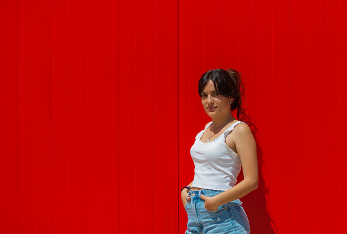 teenage girl in tank top, leaning against a red wall, with space for text.