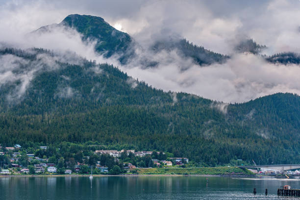 Juneau, Alaska, USA - July 19, 2011: Gray clouds captured in valley between 2 green pine covered mountains on Douglas Island. Neighborhood on shoreline Gastineau Channel. On ramp of bridge.