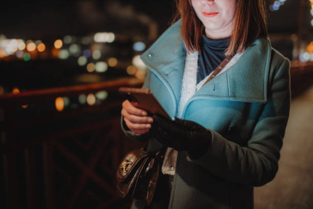 Woman in warm clothing text messaging using mobile phone outdoors in city at night