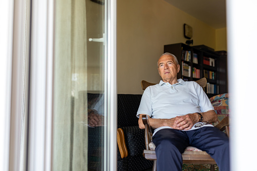 Portrait of senior man sitting on chair and looking through the window