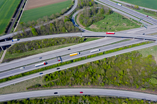 A large, curvy highway junctions with cars and trucks in spring/summer, aerial view.