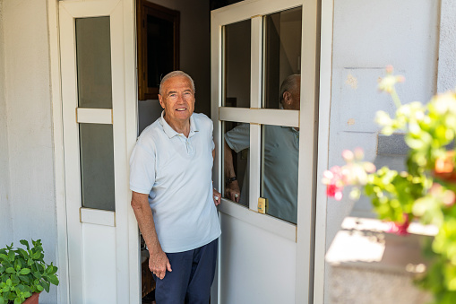 Portrait of senior man opening the front door of house, he's looking at camera