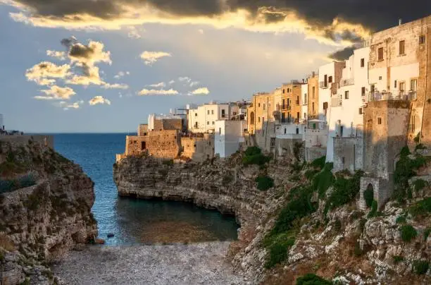 Polignano a mare, Puglia, Italy. August 2021. Amazing aerial view of Cala Monachile: the picturesque and fascinating beach of the historic center. At sunset, the golden hour, people enjoy the place.