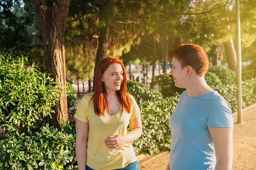 two great friends chatting and strolling happily, in a public park in the city at dawn. young girls enjoying the summer outdoors. concept of friendship and companionship. urban environment, natural light.