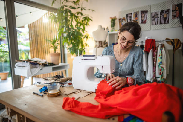 Seamstress Working on Sewing Machine Photo of beautiful smiling young seamstress working on sewing machine in her studio woman tailor stock pictures, royalty-free photos & images
