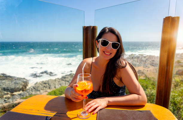 young woman sitting outdoors in resort happy drinking juice or drink with the ocean in the background young woman sitting outdoors in resort happy drinking juice or drink with the ocean in the background chile tourist stock pictures, royalty-free photos & images
