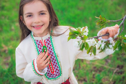 Happy beautiful girl enjoying blooming spring trees in apple orchard. Bulgarian woman in folklore dress on field.