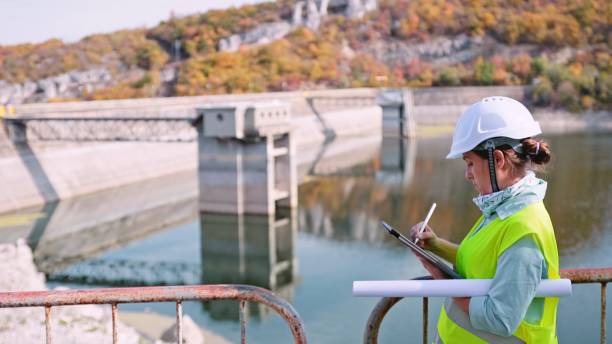 Maintenance female engineer working in hydroelectric power station. Renewable energy systems. Working day on a hydroelectric power plant. Checking the condition of the power equipment, and analysing the data and the results of measurements with a mobile app. ecologist stock pictures, royalty-free photos & images