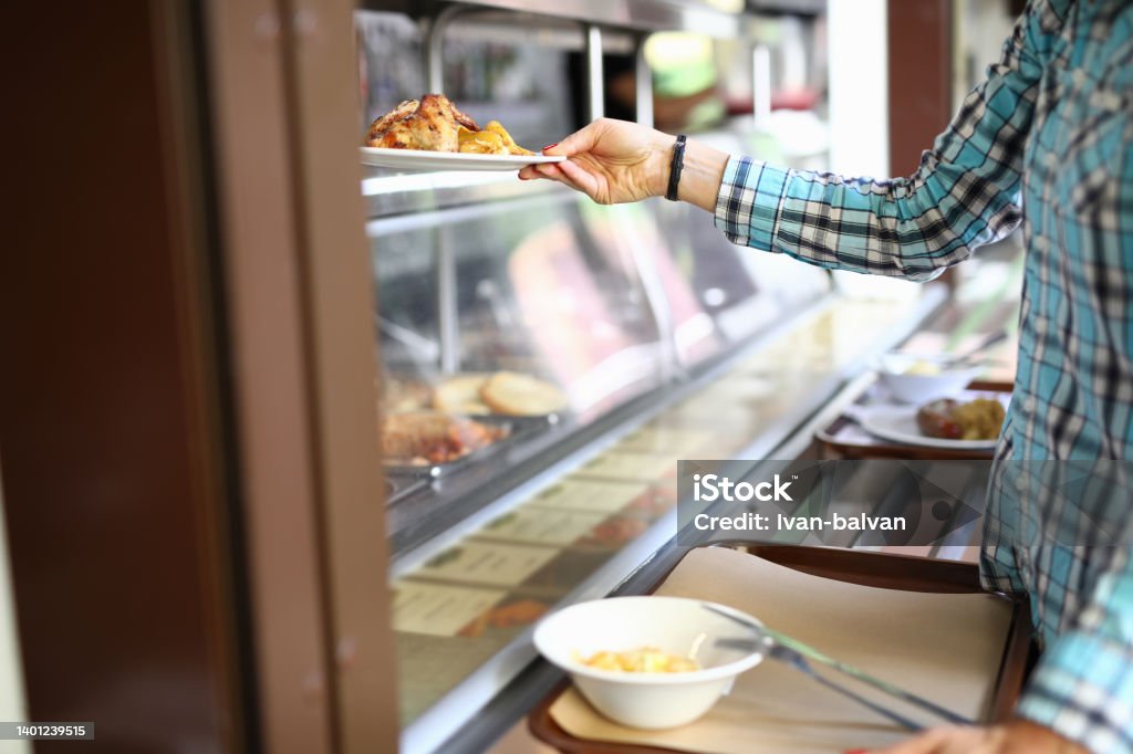 Woman taking plate with lunch in canteen Close-up of woman taking plate with lunch in canteen. Visitor with tray select dish. Customer service with wide range of dishes. Self service restaurant Cafeteria Stock Photo