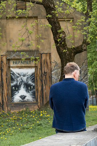 Riga, Latvia, May 21, 2022 A man sits on a wall sitting next a large cat poster.