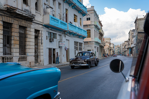 Havana, Cuba - December 8th 2022: Classic vintage cars driving along at old Havana. Old Havana is one the most unique and charming places for tourists in the world for its time-capsuled buildings and lifestyles. Some cuban students can be seen in the picture.