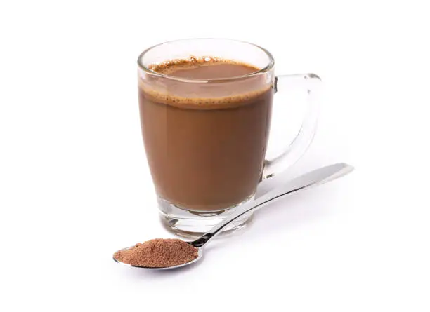 Glass mug of hot chocolate drink with cocoa powder in stainless steel teaspoon isolated on white background.