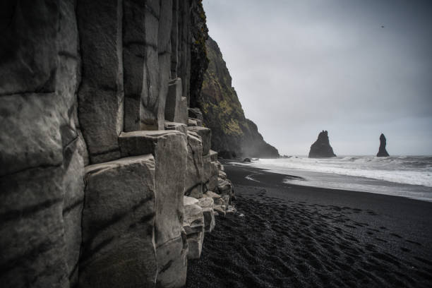 spiaggia di sabbia nera di reyinisfjara con le sue colonne di basalto e faraglioni - outcrop foto e immagini stock