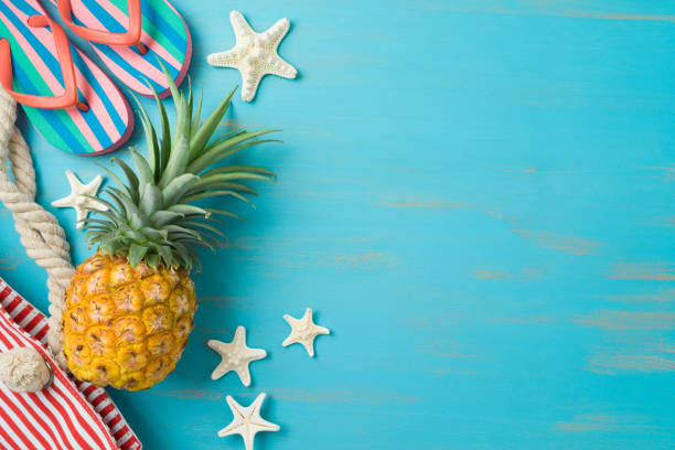 Summer beach vacation background. Pineapple, flip flips and beach bag on wooden board. Top view, flat lay