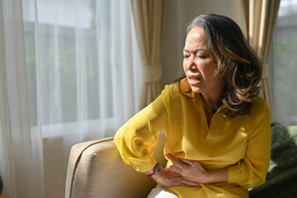 Sick asian middle aged lady hold belly suffer from abdomen ache. feeling discomfort in abdomen. stock photo