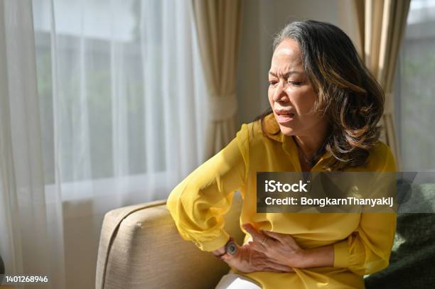 Sick Asian Middle Aged Lady Hold Belly Suffer From Abdomen Ache Feeling Discomfort In Abdomen Stock Photo - Download Image Now