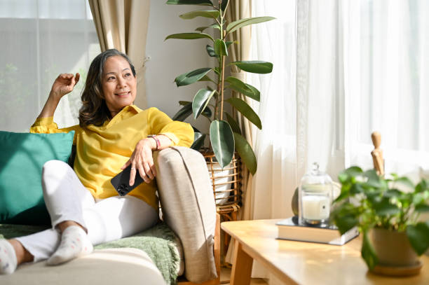 Happy asian aged woman resting in the living room, sitting on the comfortable sofa stock photo