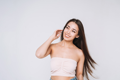 Beauty portrait of happy young beautiful asian woman with healthy dark long hair in top bando on white background isolated
