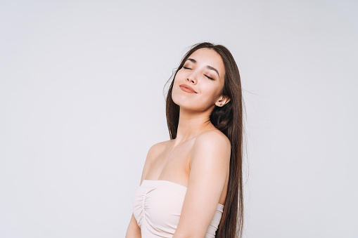 Beauty portrait of happy young beautiful asian woman with healthy dark long hair in top bando on white background isolated