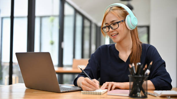 istock Woman with headphones, looking at laptop screen, writing some ideas on notebook. 1401270428