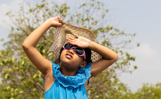 An Indian girl wearing sunglasses and holding hat looking at the Sun in summer