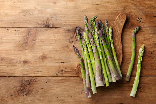 Young asparagus sticks on kitchen cutting board on wooden table top view.