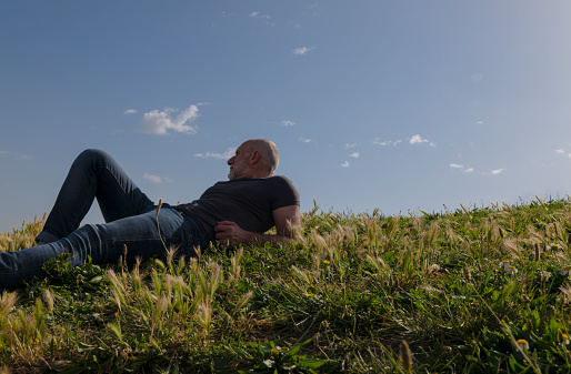 Portrait of adult man lying on grass against sky